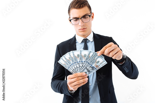 A successful businessman in glasses and a suit, holding dollar bills, carefully recalculates them on a white background. photo