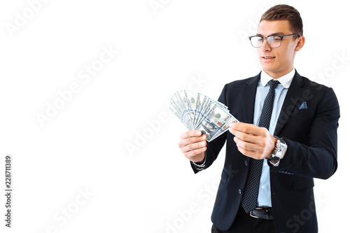 A successful businessman in glasses and a suit, holding dollar bills, carefully recalculates them on a white background.