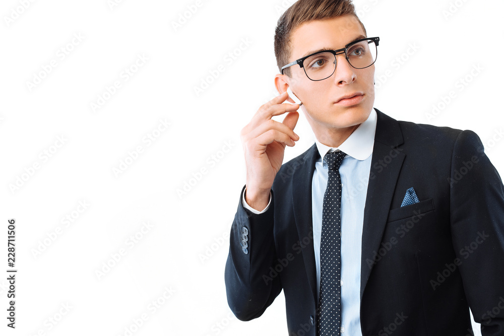 Businessman in glasses and suit, in wireless headphones, touching the earphone, on white background Businessman in glasses and suit, in wireless headphones, touching the earphone, on white background