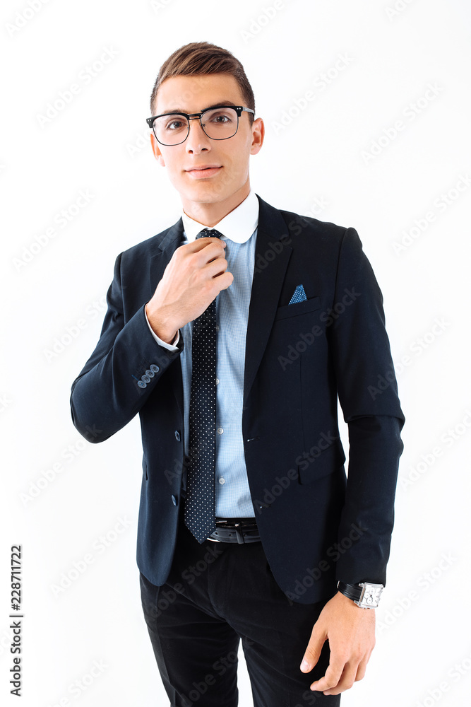 A successful businessman wearing glasses and a suit, straightens his tie and posing on an isolated white background A successful businessman wearing glasses and a suit, straightens his tie and posing on an isolated white background