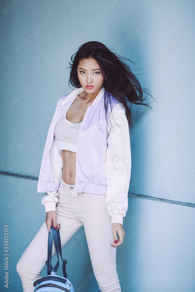 Woman Trendy Fashion. Attractive sporty asian girl in full length with  elegant hairstyle and perfect soft colorful makeup. Female with perfect  slim body in sport trendy clothes against fancy wall on Photos