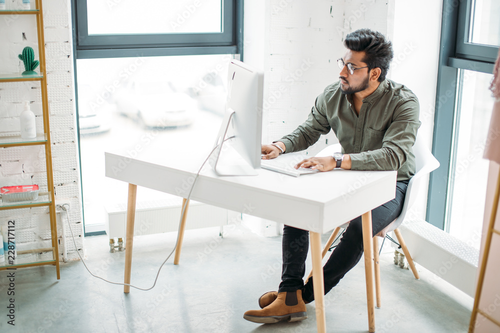 Fotografie young indian man working at computer from modern bright office