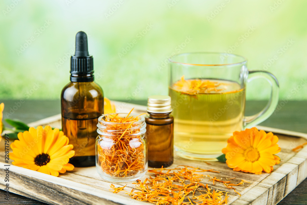 Calendula officinalis, the pot marigold, ruddles, common marigold or Scotch marigold different health products on wooden tray, essential oil, tincture, herbal tea, fresh and dried blossoms fresh green Calendula officinalis, the pot marigold, ruddles, common marigold or Scotch marigold different health products on wooden tray, essential oil, tincture, herbal tea, fresh and dried blossoms fresh green