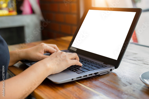 Mockup image of a businesswoman's hand using laptop with blank white desktop screen on wooden table in modern loft cafe