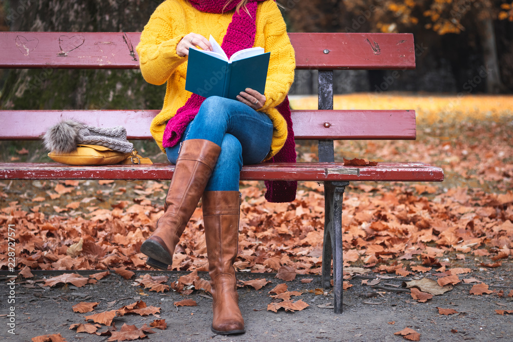 Woman sitting on bench and reading book. Autumn at public park. Woman  wearing sweater, jeans and leather boots. Photos | Adobe Stock