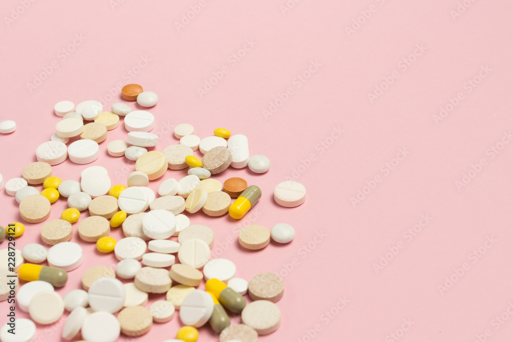 Pills of different sizes and colors on a light pink background.