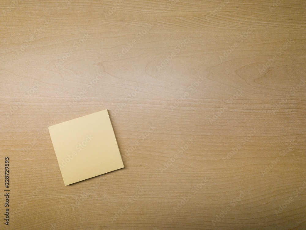 A blank yellow sticky paper pad on a wooden desk background. A blank yellow sticky paper pad on a wooden desk background.