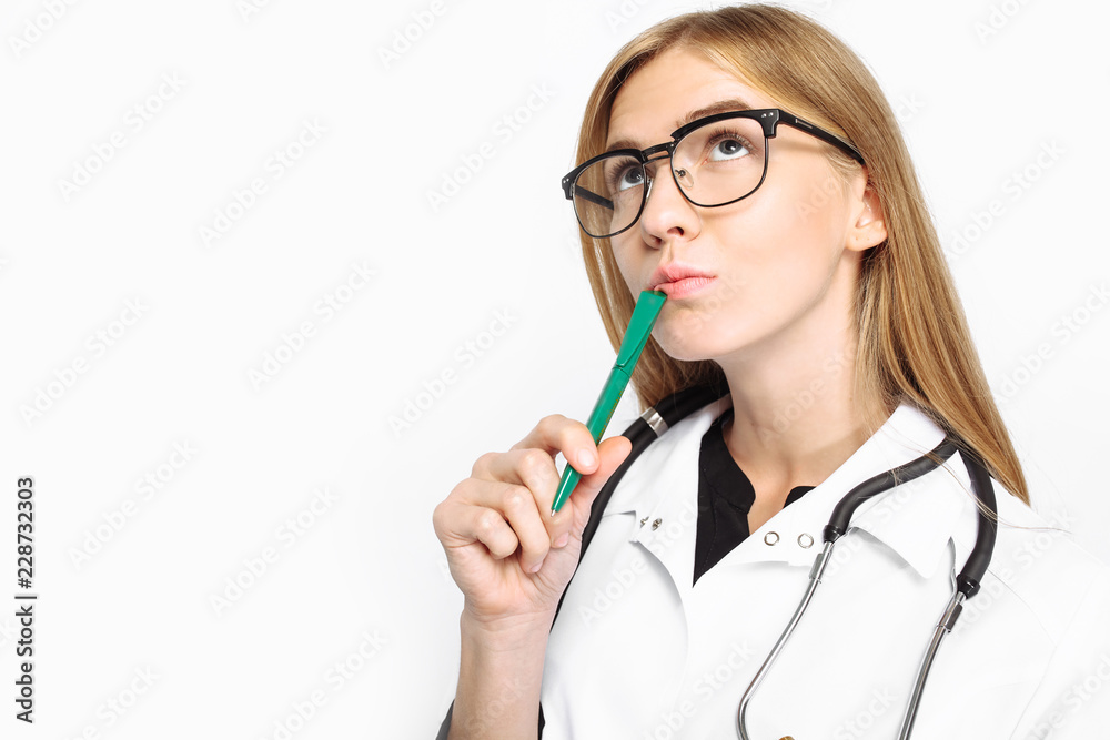 A pensive doctor, a female intern with glasses, with a stethoscope around his neck, writes the diagnosis in his folder on a white background. A pensive doctor, a female intern with glasses, with a stethoscope around his neck, writes the diagnosis in his folder on a white background.