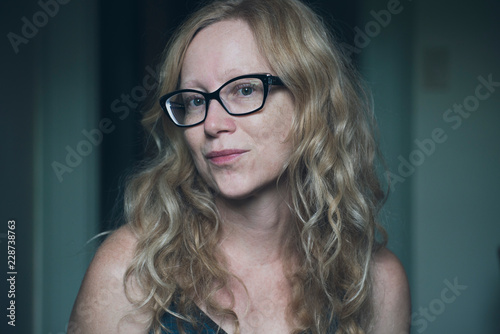 Woman with long reddish blonde wavy hair and wearing black frame glasses looks flirtatiously into the camera