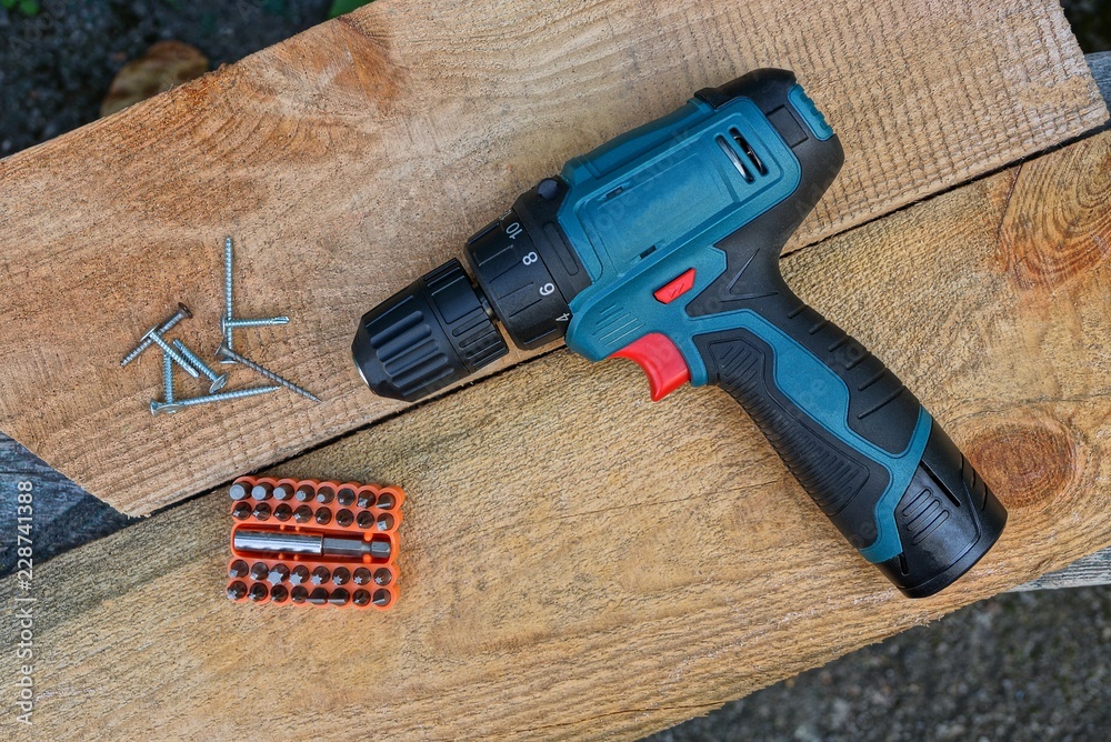 one big screwdriver and a set of bits in orange next to a pile of screws on brown wooden boards one big screwdriver and a set of bits in orange next to a pile of screws on brown wooden boards