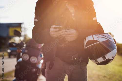 Bright shot of motorcyclist's hands with a smartphone. White helmet and a bike.