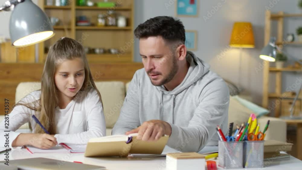 Tracking shot of caucasian father sitting at table in the living room and helping daughter with homework Tracking shot of caucasian father sitting at table in the living room and helping daughter with homework