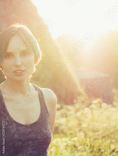Beautiful Caucasian young woman looking at the sunset with stone wall behind her. Sunset colors on her face.