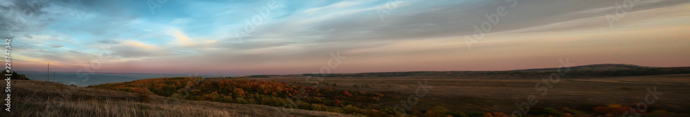 Panorama of hilly terrain with autumn forest near the Volga at sunset