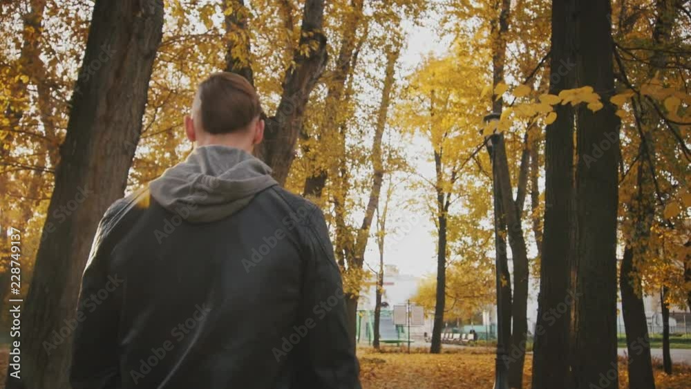 Young brutal man goes to the training session through the autumn park covered with yellow leaves. A brutal man in a black leather jacket walks through the autumn forest. Young brutal man goes to the training session through the autumn park covered with yellow leaves. A brutal man in a black leather jacket walks through the autumn forest.