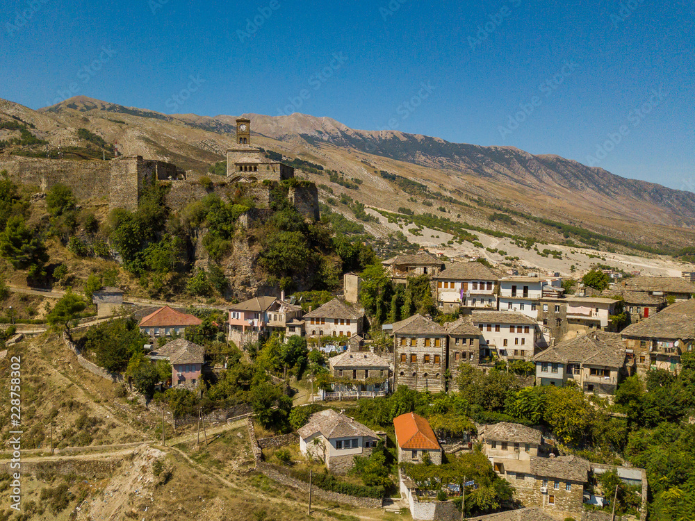Drone view of Gjirokastër Castle and city surrounded by mountains and blue sky. Also known as Kalaja, the fortress is a UNESCO heritage site in Albania
