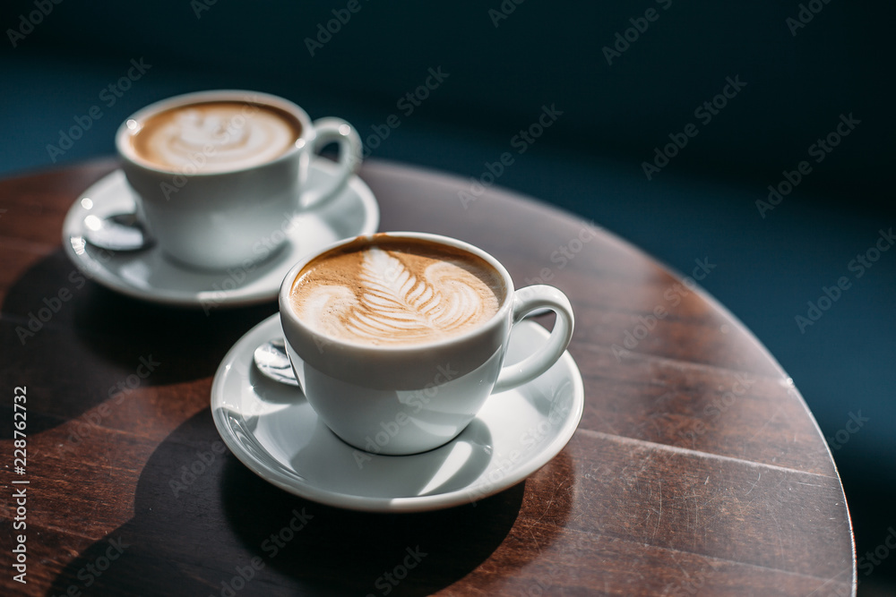 Fototapeta premium Two cups of cappuccino with latte art on wooden table. Beautiful foam, white ceramic cups.