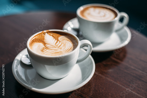 Two cups of cappuccino with latte art on wooden table