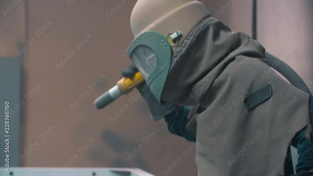 worker wearing mask using sand blast on metal surface in workshop