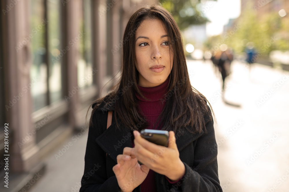 Young woman in city using cell phone walking