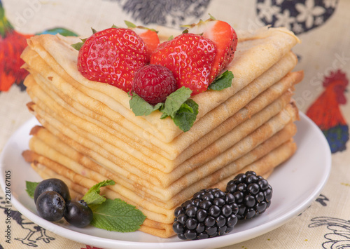Стопка блинов на блюдце с фруктами на деревенской скатерти