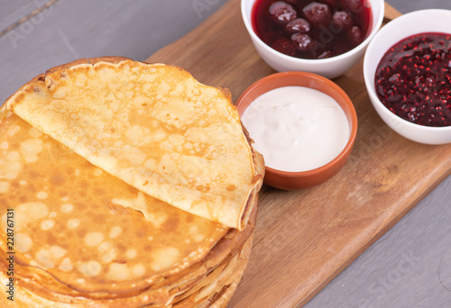 Стопка блинов на доске с вареньем и сметаной