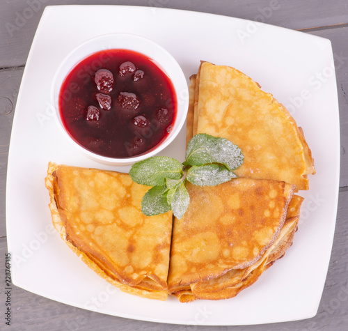 Блины с клубничным вареньем и мятой на белой тарелке