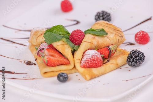 Десерт из блинов с фруктами на тарелке украшенные шоколадным соусом