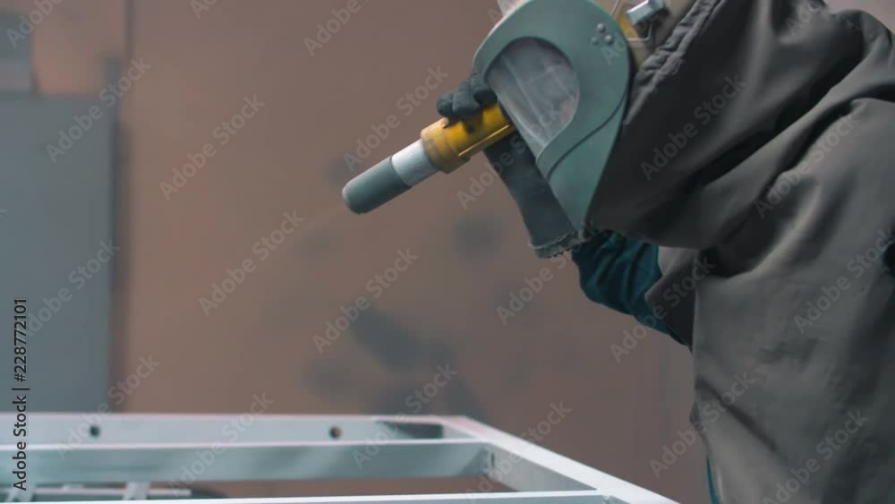 worker wearing mask using sand blast on metal surface in workshop