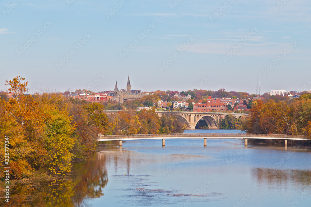 Obraz premium A view on suburban Washington DC in autumn with university buildings and bridges across Potomac River. Urban landscape on early morning with reflection in quiet river waters, Washington DC, USA.