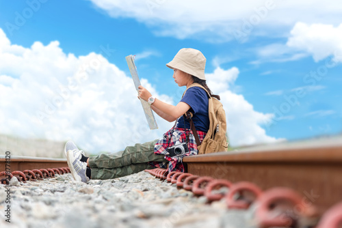 Children asian girl holding maps with camera and travel backpacks sitting in the railroad.  Travel Concept