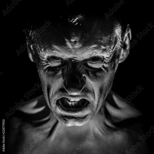 Stylish portrait of adult caucasian man with very angry face and who seems like maniac or devil. Black and white shot, low-key lighting.