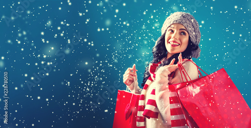 Happy young woman holding shopping bags in a snowy night