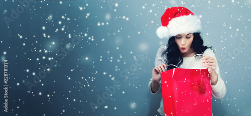Happy young woman with santa hat holding a shopping bag on a gray background