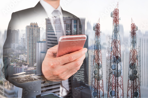 Double exposure of businessman use smartphone, communication tower or 4G 5G network telephone cellsite and foggy cityscape urban background as business, technology and telecom concept