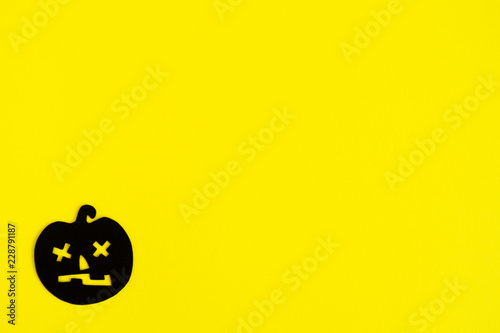 Holiday decorations for Halloween. Black paper pumpkin in the bottom left corner on a yellow background, top view.