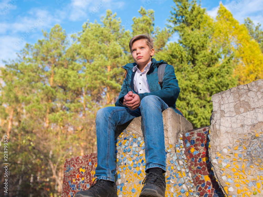 Teenager sitting on top of a rock. Autumn forest and blue sky background Teenager sitting on top of a rock. Autumn forest and blue sky background