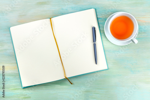 An overhead photo of an open journal notebook with a pen and a cup of tea, shot from above, a diary on a teal blue background with a place for text photo
