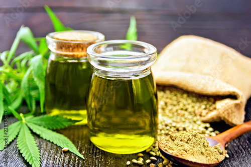 Oil hemp in two jars and flour in spoon on wooden table