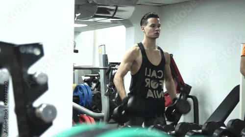 Fat funny man is picking up the smallest dumbbells next to a young handsome athlete picking up big dumbbells, both are very tired