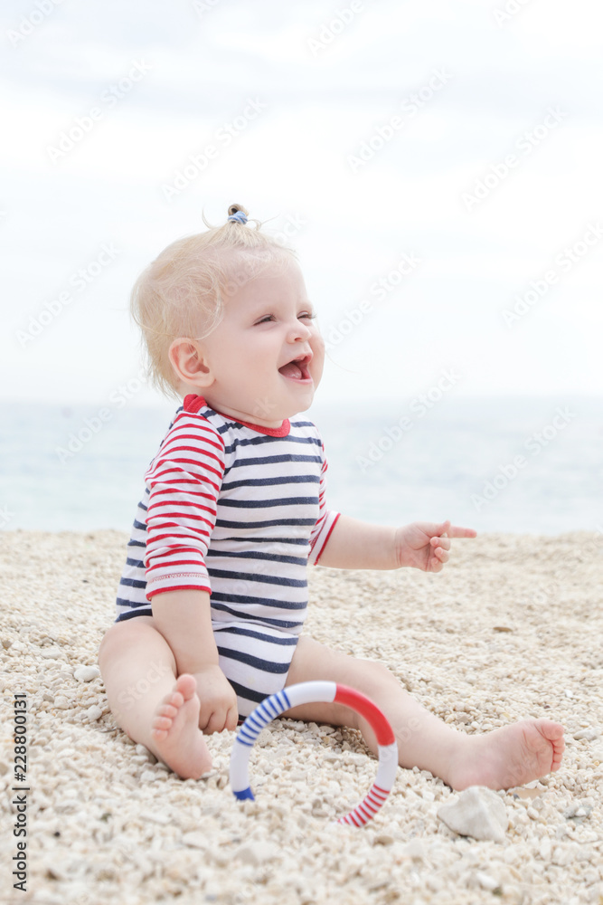 Adorable cheerful baby in striped bodysuit playing on the pebble beach Adorable cheerful baby in striped bodysuit playing on the pebble beach