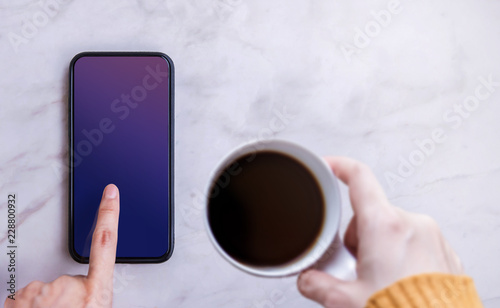 Smartphone Mockup Image. Screen as Clipping Path. Woman Touching on a Display while Drinking Coffee, White MarbleTable, Top View photo