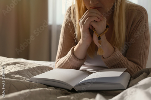 Religious young woman praying over Bible in bedroom