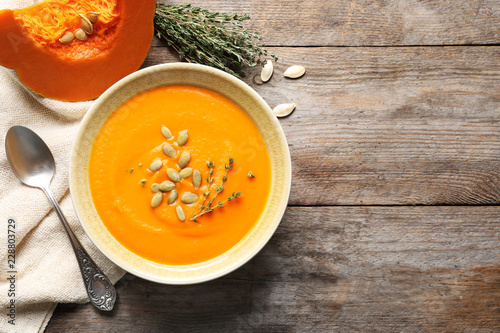 Flat lay composition with bowl of pumpkin soup and space for text on wooden background