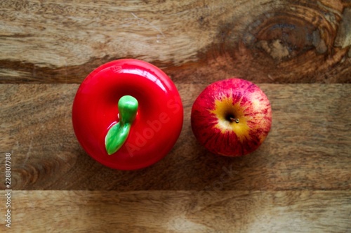 Fresh apple and ceramic apple side by side on wooden background.