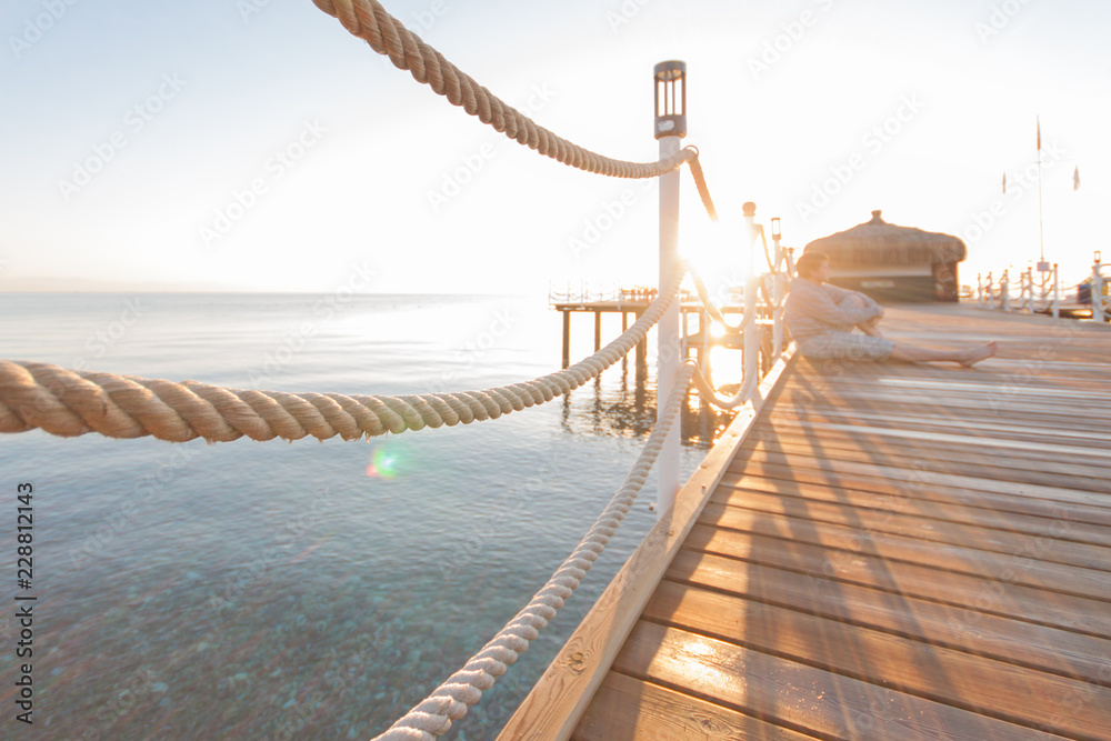 Fototapeta premium wooden pier sun-drenched, sunset or dawn, the silhouette of a man on a writing in the rays of the sun