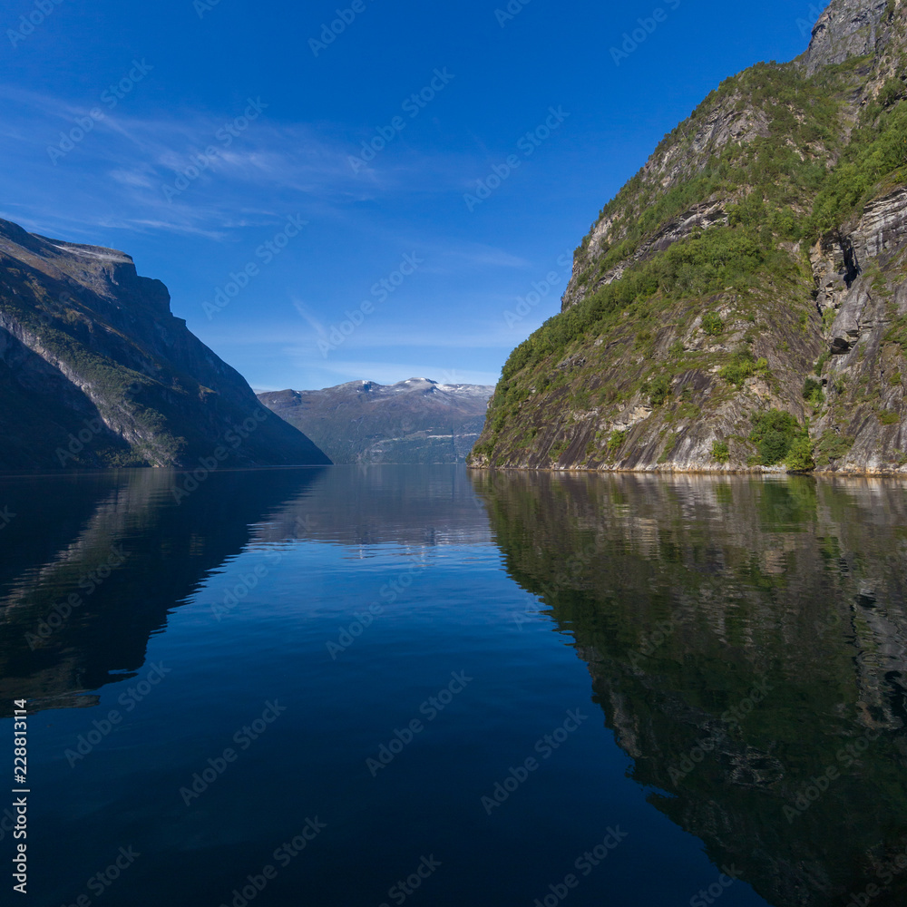 mountains reflected in Geiranger fjord, blue sea, sky