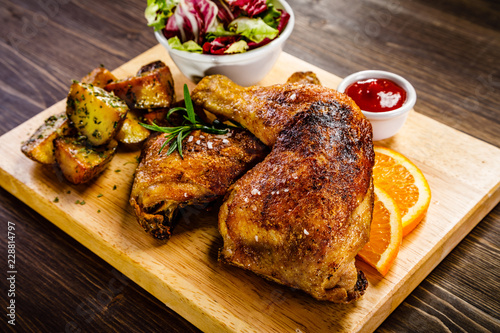 Grilled chicken legs with baked potatoes and vegetable salad on wooden table