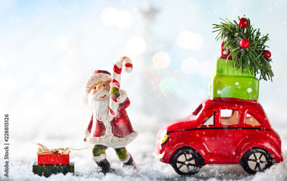 Santa Claus and red toy car carrying Christmas gifts in snowy landscape.