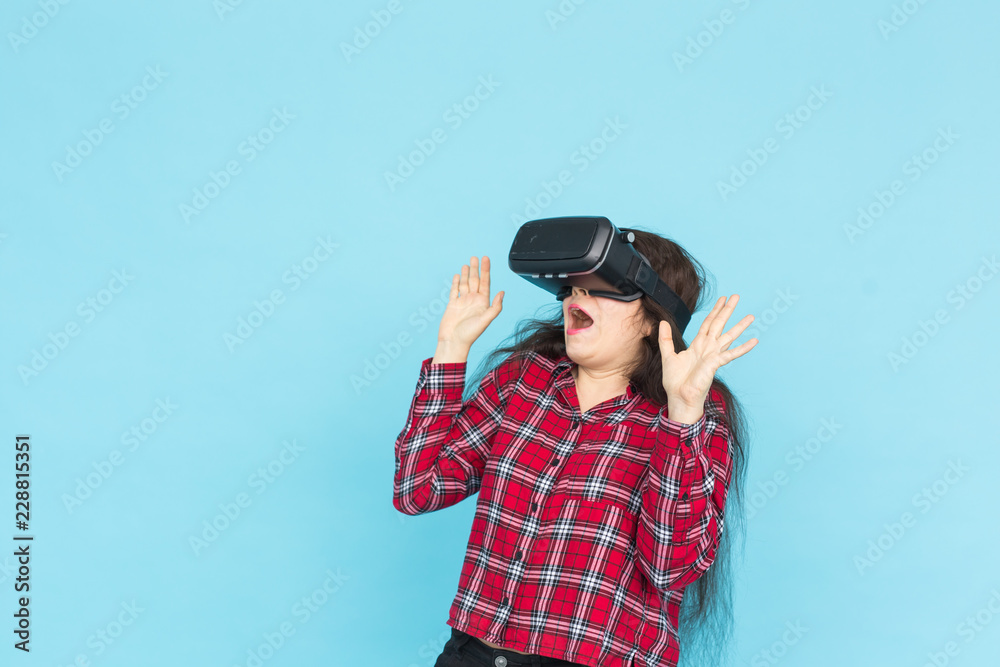 Technology and people concept - Young woman testing vr-glasses with hands up on blue background. Technology and people concept - Young woman testing vr-glasses with hands up on blue background.